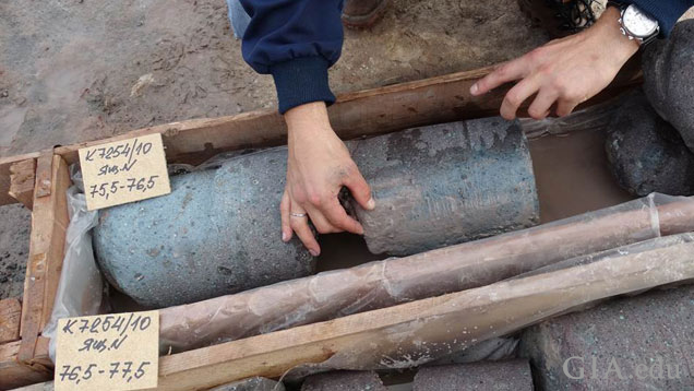Large cylindrical pieces of kimberlite pipe are laid out in wooden boxes for geologists to examine.