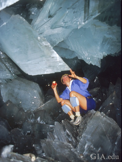 Woman sits amidst sharp, huge crystals in a cave.