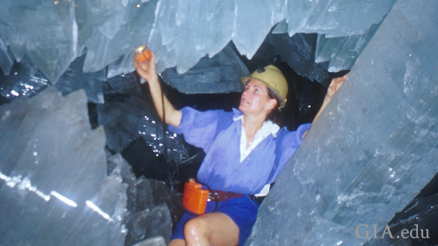 Woman shines a light on huge crystals as she crawls among them.