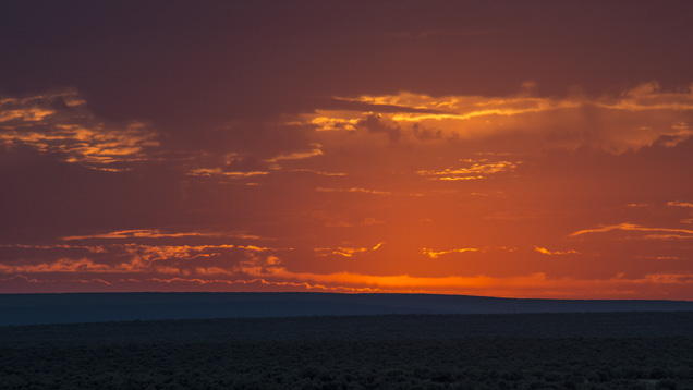 The orange glory of the setting sun hovers above a rich high-desert landscape. - Robert Weldon