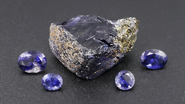 Figure 12. Rough and cut iolite from Blue Bear. From left to right, the faceted stones weigh 1.24, 0.48, 0.48, and 0.88 ct. Photo by Philippe Belley.