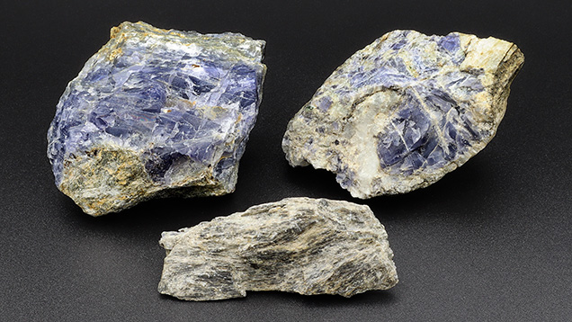 Figure 9. Representative cordierite (top left), quartz with cordierite (top right), and gedrite (bottom) from Blue Bear. As is common in metamorphic gem deposits, only a small fraction of the mineral occurs in gem quality. The gedrite fragment measures 65 mm across. Photo by Philippe Belley.