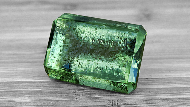 Figure 2. Rectangular step-cut green beryl from the Volyn pegmatite, 190.00 ct and 28.55 × 39.02 × 21.71 mm, with a rough unpolished table containing etch pits. Faceting and photo by Konstantyn Zalizko.