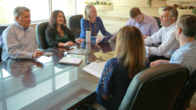 Seven people sit around a table in a meeting.