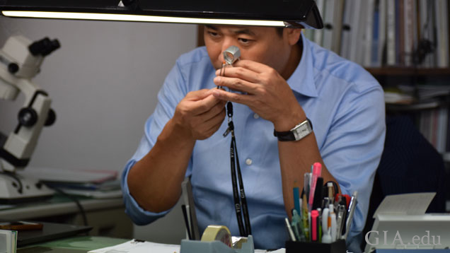 Dr. Ken Fujita uses a loupe to examine a gemstone at his desk.