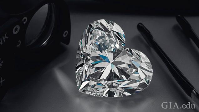 The 92 carat D flawless heart-shaped diamond is displayed next to a jeweler’s loupe and tweezers.