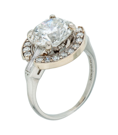Top view of a platinum solitaire ring containing a round brilliant center diamond and baguette side diamonds. A white gold halo set with small round 