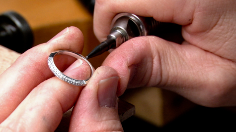 Jeweler using a hammer handpiece to check for loose stones on a pave-set diamond band