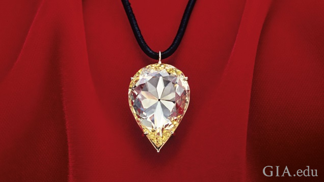 A large pear shaped yellow diamond hangs from a black cord and lies against red material.