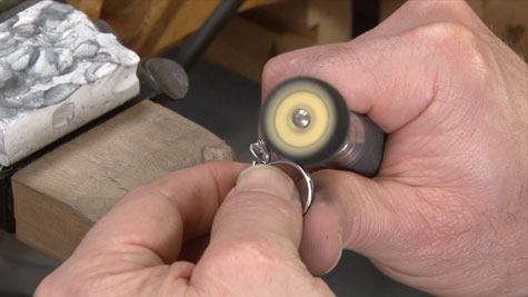 A jeweler using a smaller wheel to polish a platinum ring at the bench