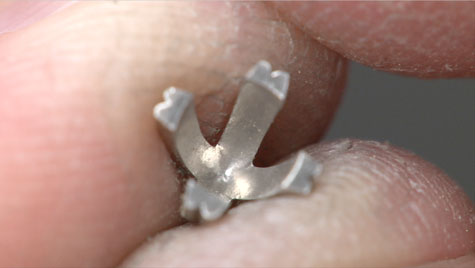 Jeweller holding the setting of a four-prong, platinum solitaire with no centre stone. The inside of the setting is visible.