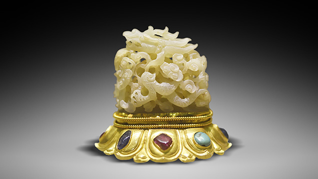 White nephrite carved jade dragon sits on a gem-inlaid gold base.