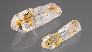 Figure 1. These two quartz crystal scepters containing a multitude of complex petroleum fluid inclusions (left) that fluoresce yellow to blue to long-wave UV light (right) are from a new deposit in Madagascar. The larger crystal weighs 11.05 ct and measures 22.81 mm in length. Photos by Annie Haynes; courtesy of Hidden Gem Gallery.