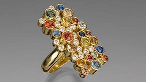 Figure 1. The “Seven Sisters” ring in 18K gold with 17 bezel-set diamonds (0.55 carats total) and 22 sapphires ranging in size from 2.5 to 4.0 mm in blue, orange, mandarin, pink, and green (3.15 carats total). Photo by Robert Weldon; courtesy of Sean Hill Designs.