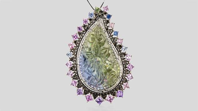 Figure 2. An 18K white gold pendant containing a paisley-shaped unheated tanzanite with a lotus blossom carving, surrounded by pav&eacute;-set black diamonds and pink and purple princess-cut Sri Lankan sapphires. The total weight of the diamonds is 1.00 carats, and the colored stones total 23.40 carats. Photo by Robert Weldon; courtesy of YNY Jewels Inc.