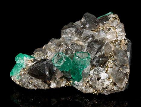 Figure 2. In sample 17 (26 mm in length), a base of black shale (not visible) is covered with numerous albite, calcite, and pyrite crystals. In this matrix, five emerald crystals are embedded, two of them developed in the form of empty cups. The emerald cup on the right is 5.5 mm long. Photo by G. Martayan.