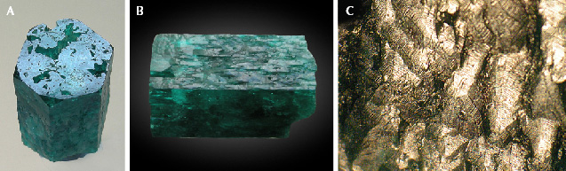 Figure 5. Sample 2 (18.0 mm in length), a columnar emerald that has been heavily corroded by natural etching. A: The basal plane shows irregularly shaped openings to larger cavities below this face. B: The <em>m</em> prism planes show etch structures, especially irregularly oriented grooves between hillocks. C: Details of the etch structures with grooves and hillocks, seen on the <em>m</em> prism face in image B, which are covered by micro-steps as seen in reflected light. Photos by K. Schmetzer; field of view 3.5 mm (C).