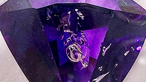 This 16.60 ct triangular-shaped enhydro amethyst, measuring 17 × 19 mm, contains a large primary fluid inclusion with a free-moving gas bubble prominently oriented in the center of the table. Photo by Lisa Kennedy; courtesy of Gem & Gold Creations.