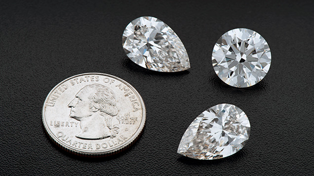 Figure 1. Three large CVD-grown diamonds submitted by Plasmability to GIA for scientific examination: A matching pair of pear-cut gems weighing 8.88 and 8.89 ct, as well as a 10.13 ct round brilliant. These American-grown diamonds are displayed with a U.S. quarter (24.26 mm diameter) for scale. Photo by Jian Xin (Jae) Liao.