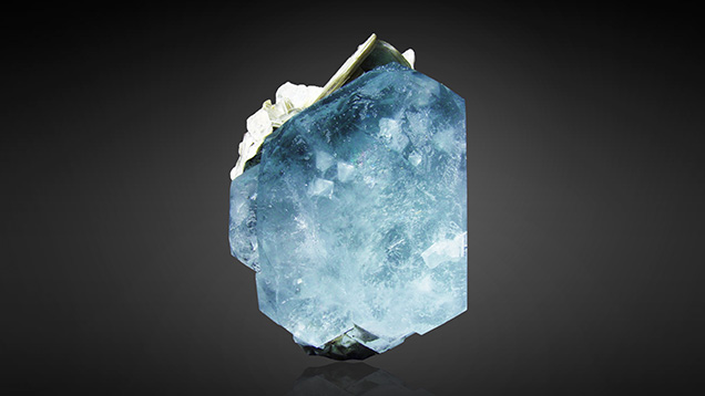 Figure 1. Twelve white octahedral fluorite crystals ranging from 5 to 10 mm across are visible inside this well-formed aquamarine crystal. Photo by Russell E. Behnke.