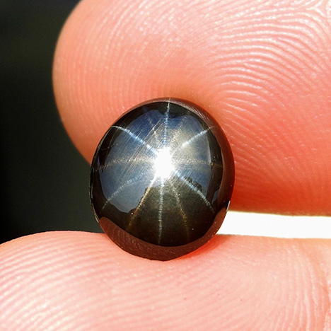 A black star sapphire with one set of golden rays and another set of silver rays.