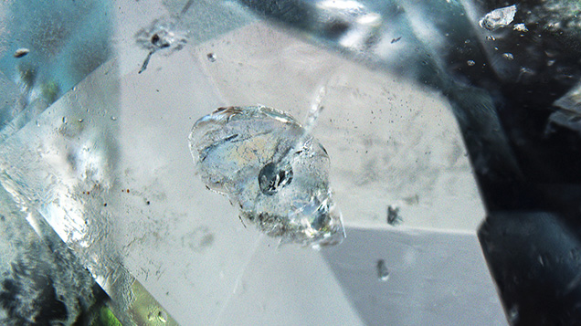 Figure 3. Disk-shaped fissures in the aquamarine were caused by solid inclusions in the middle with tubular fissures extending inward. Photomicrograph by Yubing Chen; field of view 1.50 mm.