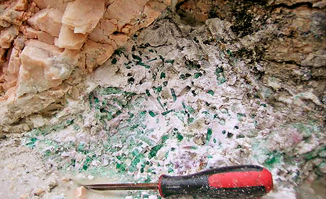 Figure 11. Colored tourmaline crystals embedded in secondary clay minerals in a pocket at the Havey pegmatite near Poland, Androscoggin County, Maine, in July 2018. Courtesy of William (Skip) Simmons.