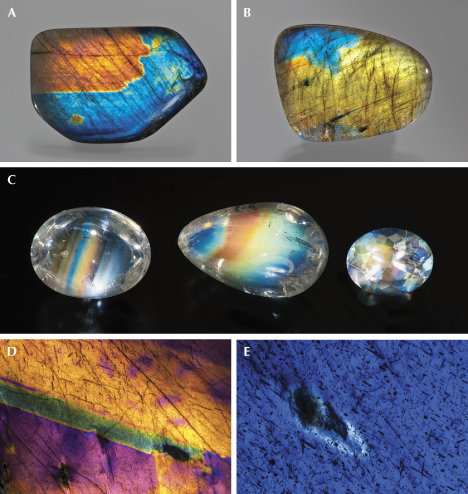 Figure 28. A and B: Labradorite from Finland (28.05 × 42.66 mm) and Madagascar (23 × 35 mm), respectively, showing iridescence close to the surface; courtesy of Black Star Trading Company. C: The iridescence of Zambian “rainbow moonstone” labradorite (largest 2.82 ct) comes from much deeper inside the stone due to its high transparency; gift of Scott Davies. D: Labradorite from Finland is heavily clouded with opaque inclusions that block light from traveling deep into the crystal, so the iridescence appears as a coating on the surface. E: Higher magnification reveals that the opaque inclusions are floating over the blue iridescence, indicating that the interference color always arises from inside the labradorite crystal. Photos by Robert Weldon (A–C) and Nathan Renfro (D and E); fields of view 18.8 mm (D) and 5.05 mm (E).