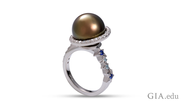 A black Tahitian pearl is encircled by a ring of diamonds. Four stars, with sapphires and aquamarines in their centers, cascade down one side of the shank.