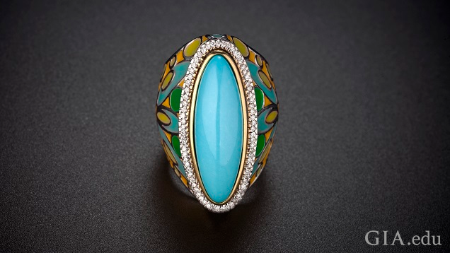 An elongated oval piece of turquoise is framed by diamonds with a enameled shank of turquoise, green, yellow and orange colors.