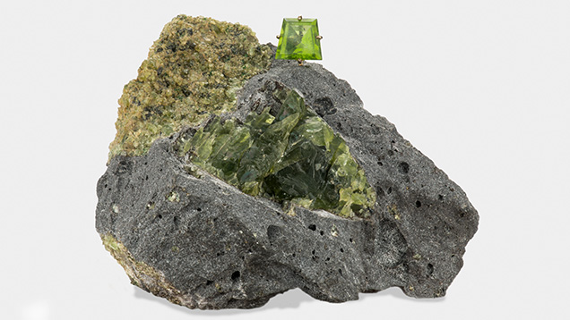 Peridot nodule in host basalt, with a faceted peridot sitting atop.