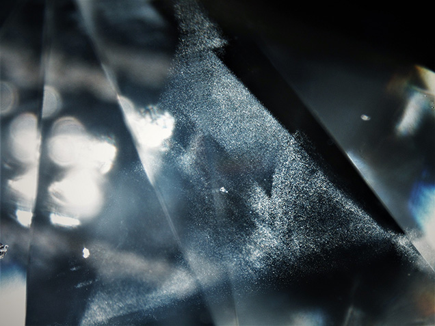 Figure 1. This particle cloud, a typical inclusion in diamond, shows an iridescent appearance and is grouped in a triangular shape viewed in fiber-optic illumination. Photomicrograph by Aprisara Semapongpan; field of view 2.8 mm.