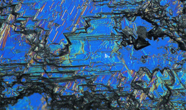 Figure 18. French Bar sill sapphires show a variety of different resorption features, also called etching or dissolution. In this sapphire (RK-FBS 041), differential interference contrast (DIC) photomicrography shows angular geometric patterns reflecting disequilibrium with the carrier magma during its volcanic transport to the surface. Photomicrograph by Aaron Palke; field of view 0.52 mm.