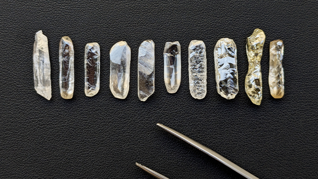 10 pale yellow baguette shaped rough diamonds against a black surface 
