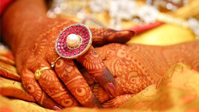 A spaceship-inspired ring of pink gems surrounding a pearl is showcased on a bride’s intricately drawn henna hands.
