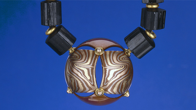 This mokume gane pendant, made of patinaed copper and 14K yellow, red and grey gold, hangs on a black tourmaline crystal bead and 22K gold rondel necklace. Mokume gane is a technique used to layer metals. Created by George Sawyer. Photo by Robert Weldon/GIA, gift of George Sawyer.