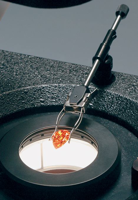 Synthetic orange sapphire held by clamp over a darkfield microscope 