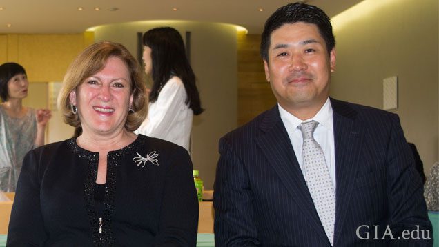 Susan Jacques and Ken Fujita, dressed in business attire, sit side-by-side at an event. 