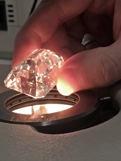 Fingers hold a very large diamond over a bright light.